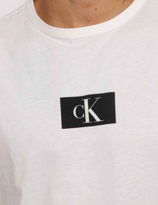 T-shirt Calvin Klein Bianco - T-shirt su sfondo bianco con stampa logo brand nero. La vestibilità è morbida e regolare. La t