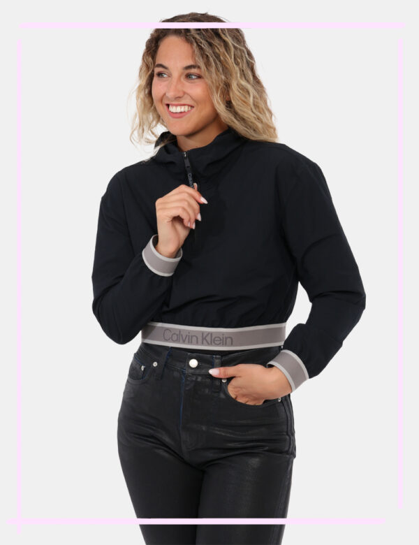 Giacca Calvin Klein Nero - Giacca a vento corta con cappuccio e zip. Presenta polsini e borso inferiore con logo Calvin Klei